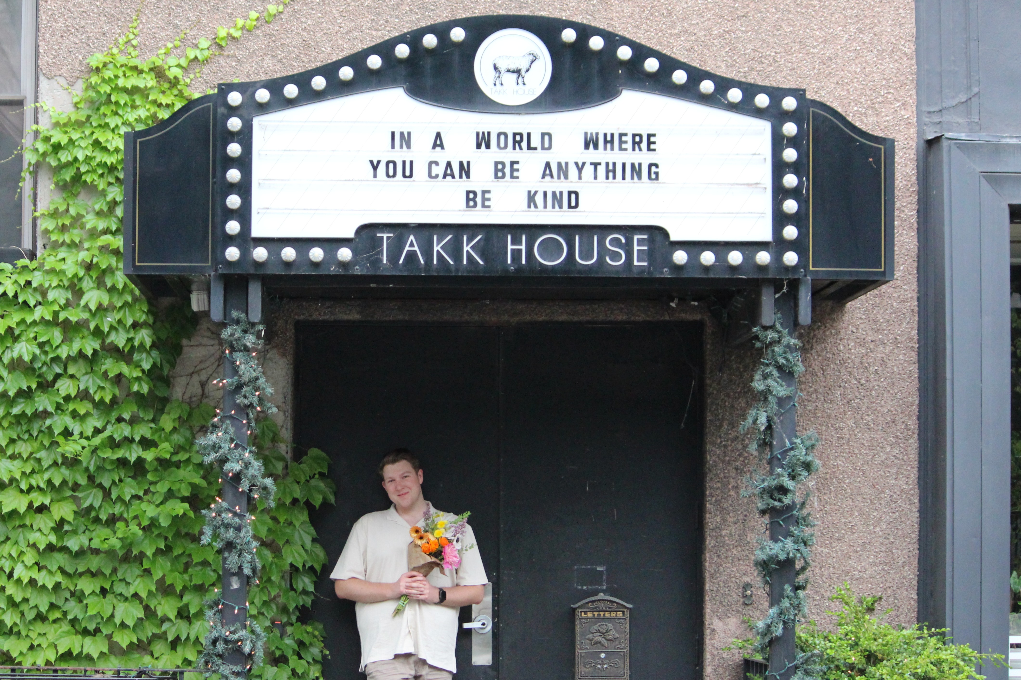 Hunter Hodge under a sign that says 'In a world where you can be anything, be king'.